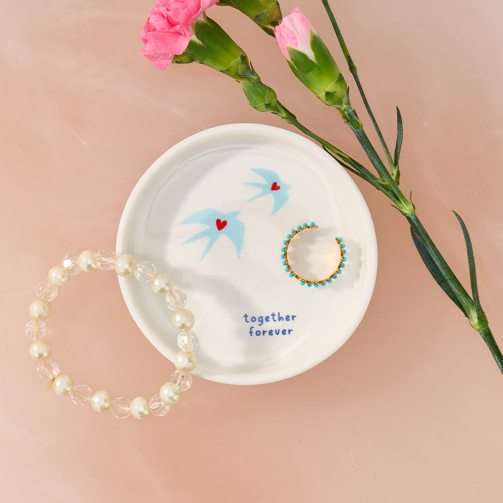 White dish with decorative elements and jewelry on a pink background