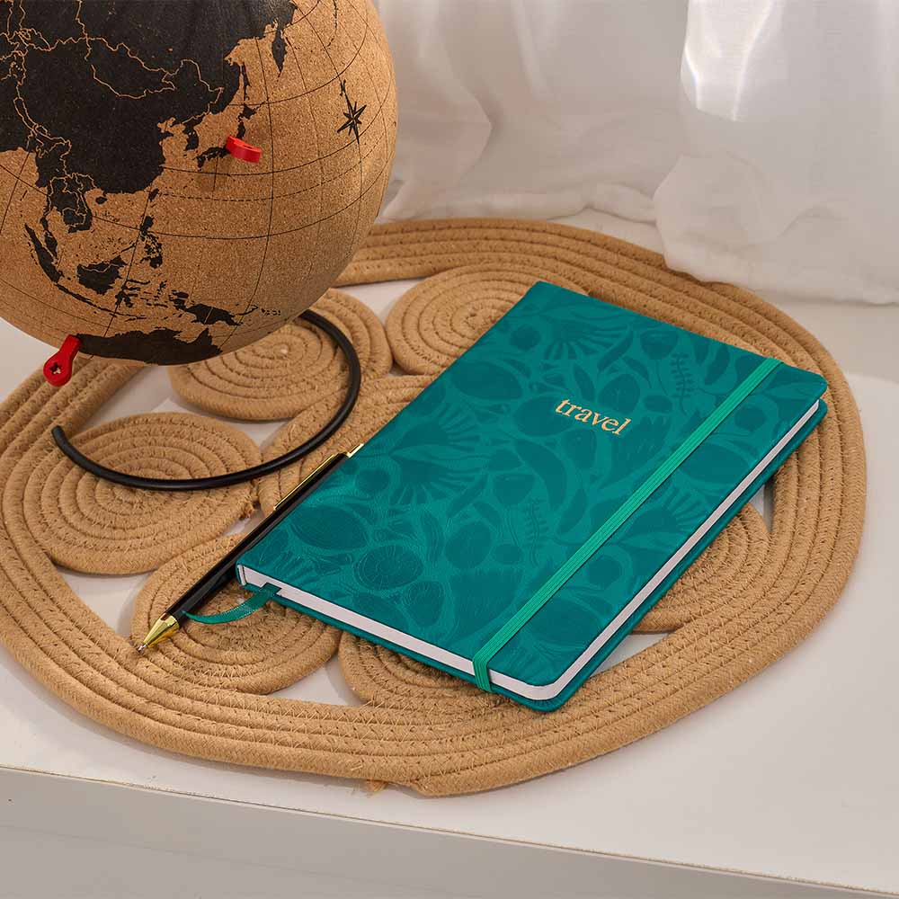 Green notebook with 'travel' on it next to a globe on a woven mat