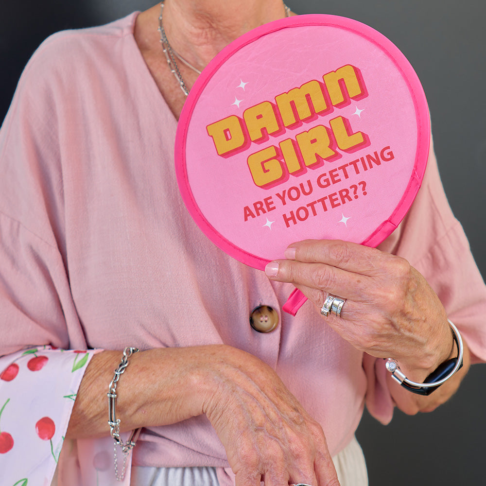 Person holding a pink twist fan with 'Damn Girl Are You Getting Hotter?' text