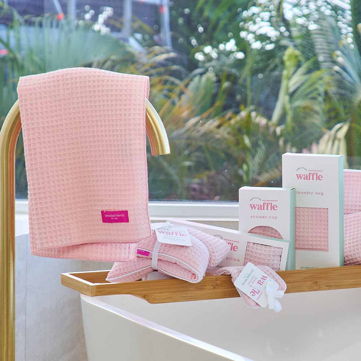 Pink waffle towel and packaging on a bathtub with a garden view