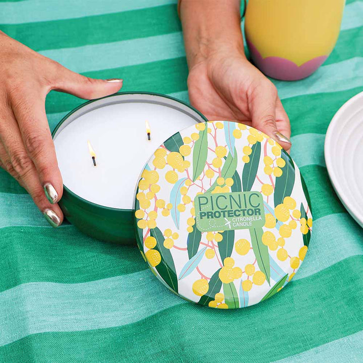 Candle with floral design lid on a green striped fabric background