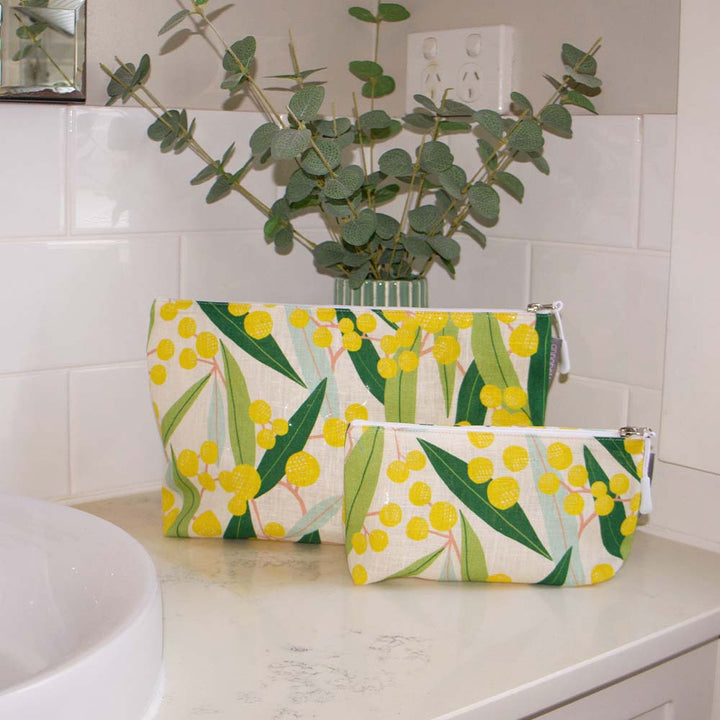 Two floral-patterned pouches on a bathroom counter with a plant in the background.