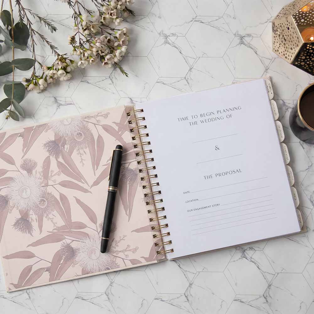 Open planner with floral design on cover, pen, and decorative elements on marble surface
