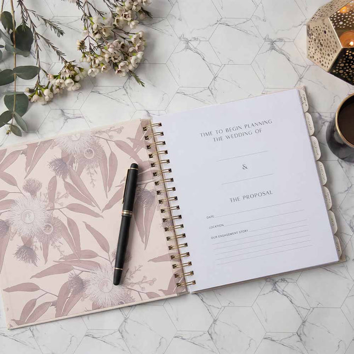Open planner with floral design on cover, pen, and decorative elements on marble surface