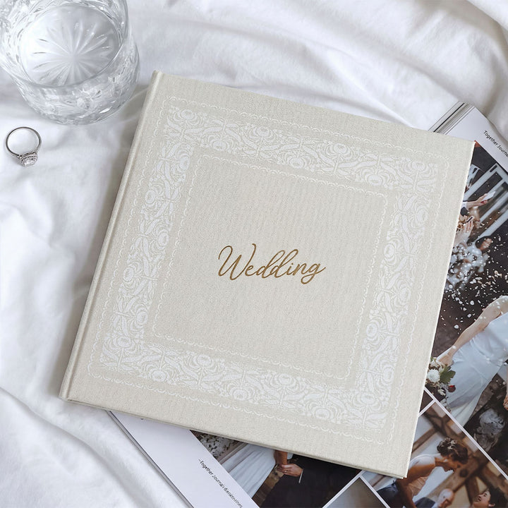Wedding album with decorative cover on a white surface with a glass and ring.