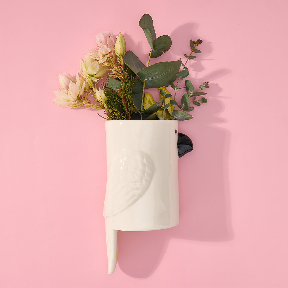 White cockatoo-shaped vase with flowers on a pink background