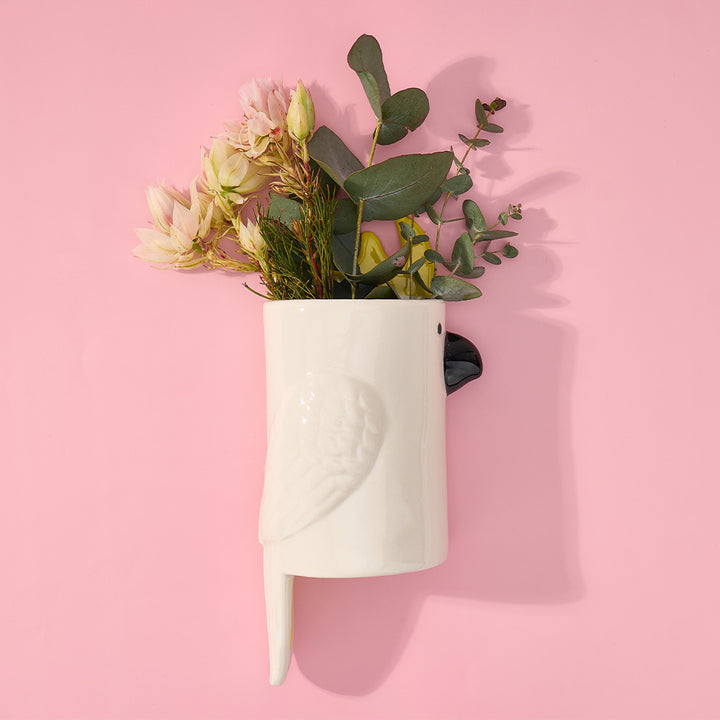 White cockatoo-shaped vase with flowers on a pink background
