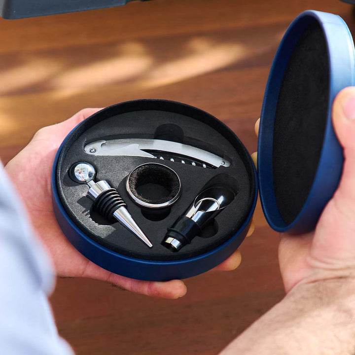 Set of wine accessories including a bottle opener, cork screw, and stopper in a blue box held by hands.