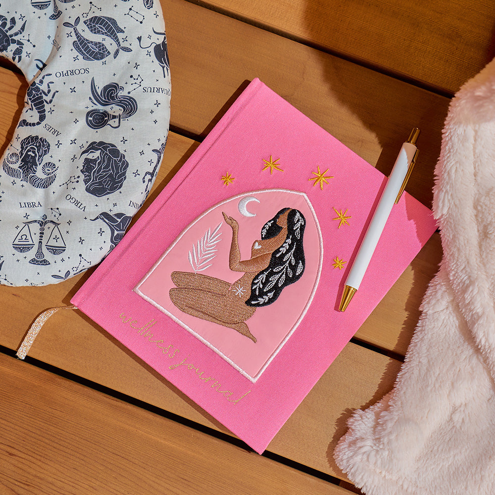 Pink notebook with an embroidered woman illustration on a wooden surface
